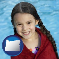 oregon map icon and a little girl wrapped in a dark red towel, in front of a swimming pool