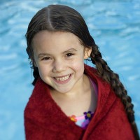 a little girl wrapped in a dark red towel, in front of a swimming pool