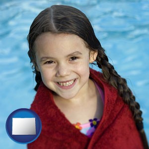 a little girl wrapped in a dark red towel, in front of a swimming pool - with Colorado icon