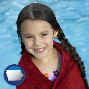 a little girl wrapped in a dark red towel, in front of a swimming pool - with Iowa icon