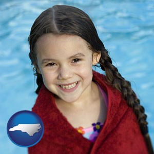 a little girl wrapped in a dark red towel, in front of a swimming pool - with North Carolina icon
