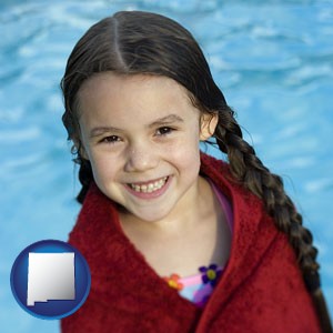 a little girl wrapped in a dark red towel, in front of a swimming pool - with New Mexico icon