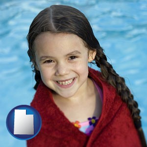 a little girl wrapped in a dark red towel, in front of a swimming pool - with Utah icon